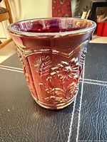 Front view of deep red iridescent carnival glass vase with floral embossing