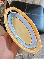 Top view of oval porcelain tray showing yellow rim, blue band, cream center, handles