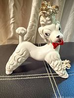 Front view of white porcelain poodle figurine with red bow and gold accents
