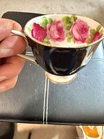 Side view of teacup showing black exterior, foot, handle and gold trim