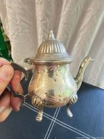 front view of silver-plated miniature teapot showing lid, handle, spout and feet