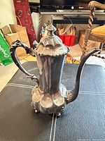 Full view of ornate silver-plated teapot, handle, spout, feet visible