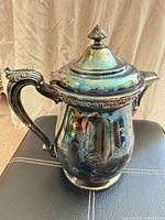 Front view of silver-plated coffee pot showing floral relief and handle