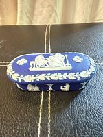 Top view of trinket box with lid showing white relief scene and laurel border