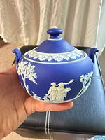 Front view of covered sugar bowl showing relief figures and lid