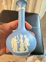 Front of light blue jasperware bud vase with white relief figures, held in hand