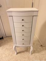 Front view of closed white jewelry armoire showing six drawers and cabriole legs