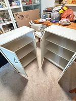 Pair of white laminate cabinets with doors open showing shelves