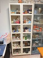 Front view of white display cabinet with doors closed, contents inside for scale