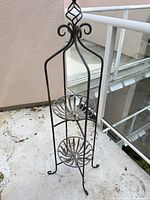 Full view of wrought iron plant stand showing two circular shelves and decorative top
