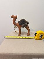Left side view of leather camel figurine, fabric saddle, tassels, measuring tape shows approx 8 in length