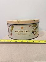 Side view of tin showing maker’s crest and measuring tape indicating ~8 in diameter