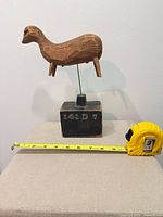 Side view of carved wood animal on stand with tape measure for scale