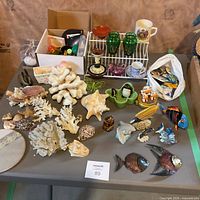 Full table view showing coral, shells, metal fish plaques, ceramic fish, glassware, porcelain cups, small trinkets