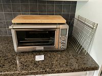 Toaster oven with bamboo cutting board on top and two wire racks leaning beside