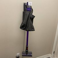 Full view of Dyson stick vacuum mounted on wall with bag and floor head visible