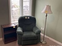 Recliner chair beside floor lamp and side table in front of window