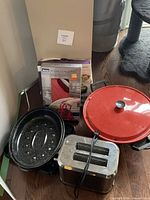 Lot overview showing toaster, roaster pans, boxed turkey lifter, red-lid skillet