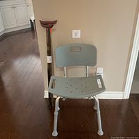 Shower chair front view with wooden cane beside it