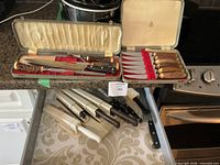 Open fitted case showing carving knife, sharpening steel and six steak knives with antler-style handles; drawer below with electric knives and loose kitchen knives