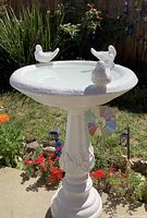 Full view of white concrete bird bath in garden setting