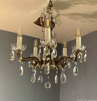 Full view of chandelier unlit showing brass arms and hanging crystals