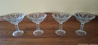Four clear glass pedestal dessert dishes aligned to show overall form and matching heart pattern