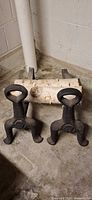 Pair of cast iron andirons on concrete floor with birch log for scale