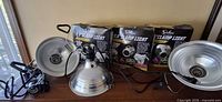 Three unboxed clamp lights with cords and clamps alongside three boxed units