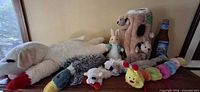 All toys lined on table including giant Lamb Chop, duck, grey plush, small lamb, bunny, trunk with squirrels, beer bottle, caterpillar