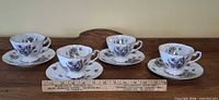 All four teacup and saucer sets lined in a row with ruler for scale