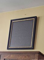Front view showing black frame with gold trim and dark grey print surface