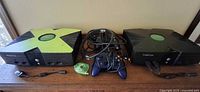 Both Xbox consoles, controllers, memory unit and cables displayed on surface