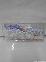 Front view of packaged white lace bridal garter with blue ribbon and pink rosette, labeling visible