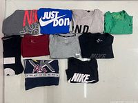 Ten folded Nike T-shirts assorted colours and graphics displayed on table