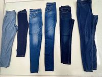 Six pairs blue denim and jegging pants laid flat