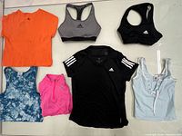 Seven Adidas and assorted tops and sports bras laid flat on surface