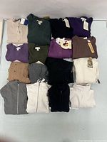 Overhead view of sixteen folded sweaters showing colours, styles and tags.
