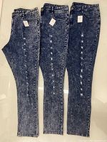 Three pairs acid-washed jeans laid flat front side up showing overall style, wash, and sizes