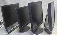 Front and side view of four black LCD monitors on stands, cables partially visible