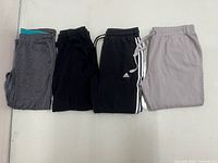 Four folded sweatpants lined side by side showing colors, stripes and logo