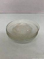 Stack of five matching clear pressed glass plates showing starburst centers and triple-ring rims