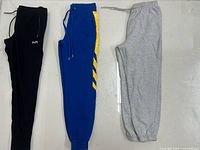 Three sweatpants in black, blue with yellow stripes, and heather gray laid flat