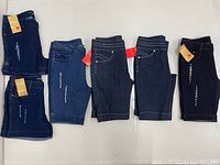 Six pairs of denim shorts laid flat showing washes, tags, and sizes