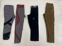 Four pairs of leggings laid flat: gray/black, gray/maroon, black Nike Pro, olive green