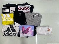Eight folded athletic T-shirts displayed on table showing logos and graphics