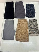 Six pairs of shorts laid flat: black, charcoal chambray, navy palm print, light grey, tan camo, green camo