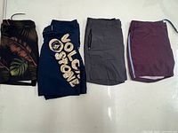 Four pairs of board shorts: black tropical leaf, navy Volcom Stone, solid grey, maroon patterned