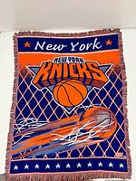 Full view of woven New York Knicks tapestry throw blanket with logo, basketball graphic, and fringed edges