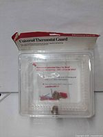 Front view of packaged Honeywell Universal Thermostat Guard showing lock, keys and hardware